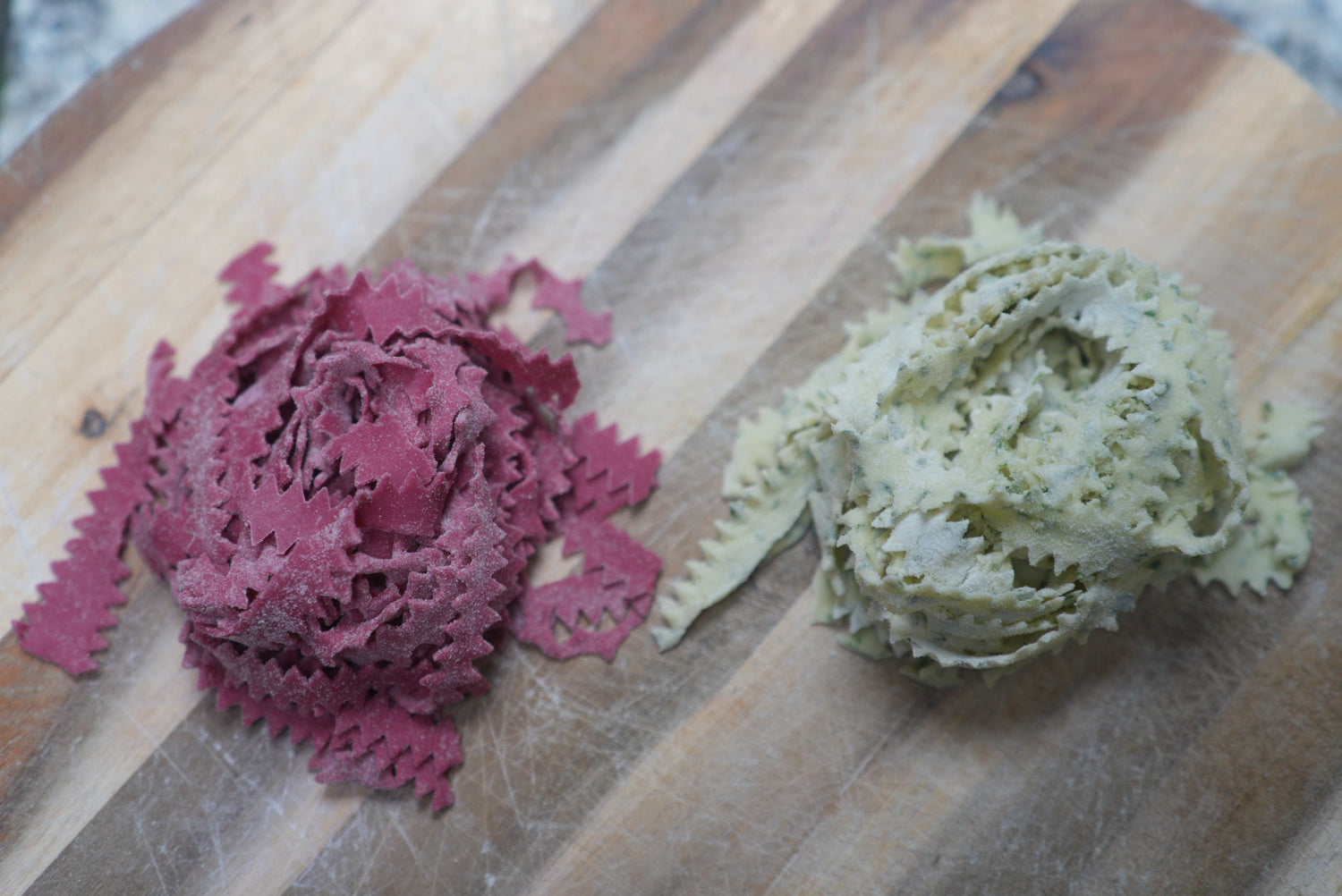 Roze tagliatelle en gespikkelde tagliatelle in een nest gedraaid op een houten plank