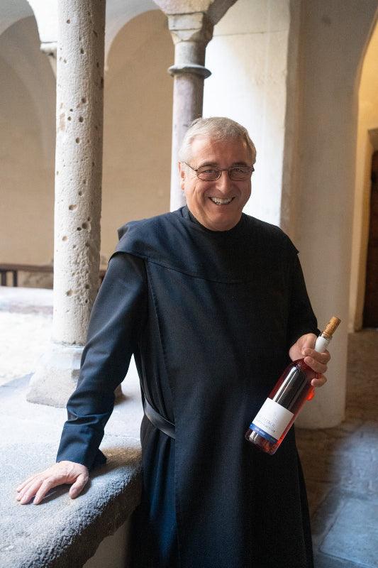 Muri Gries pater die een fles wijn vasthoudt