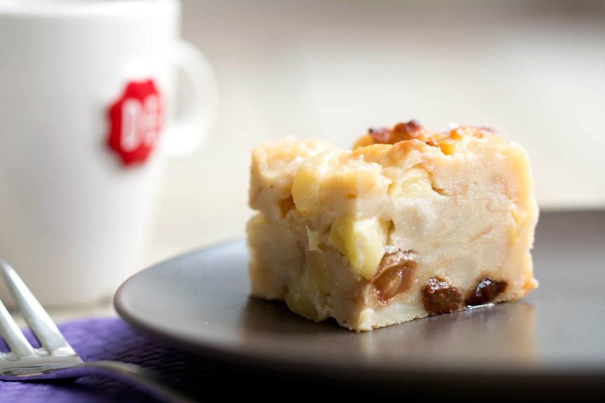 Een bordje met in de achtergrond een kopje voor koffie en vooraan ligt een rechthoekje van broodpudding