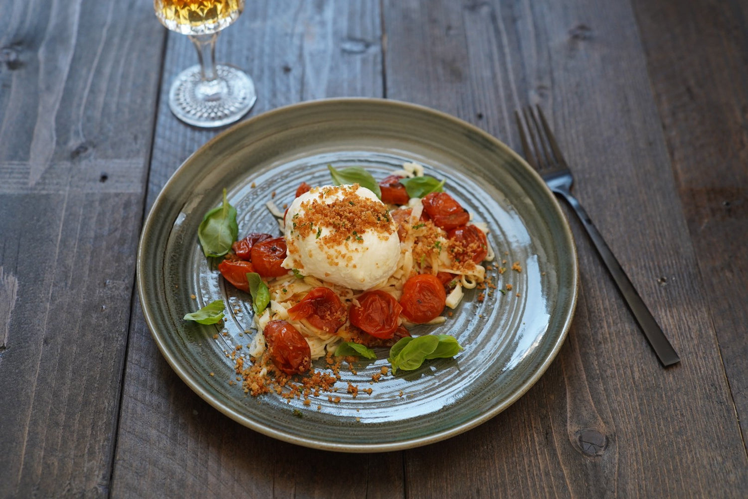 Capellini d'angelo met geroosterde tomaten, burrata en pangrattato op een bord