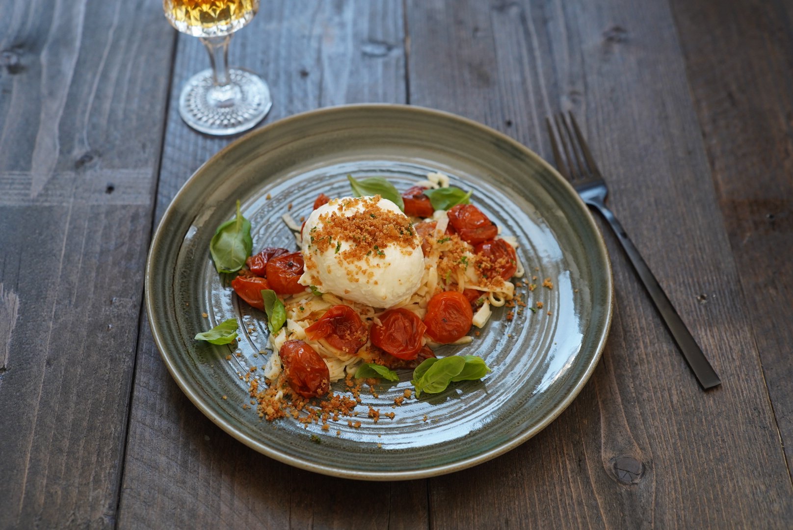 Capellini d'angelo met geroosterde tomaten, burrata en pangrattato op een bord