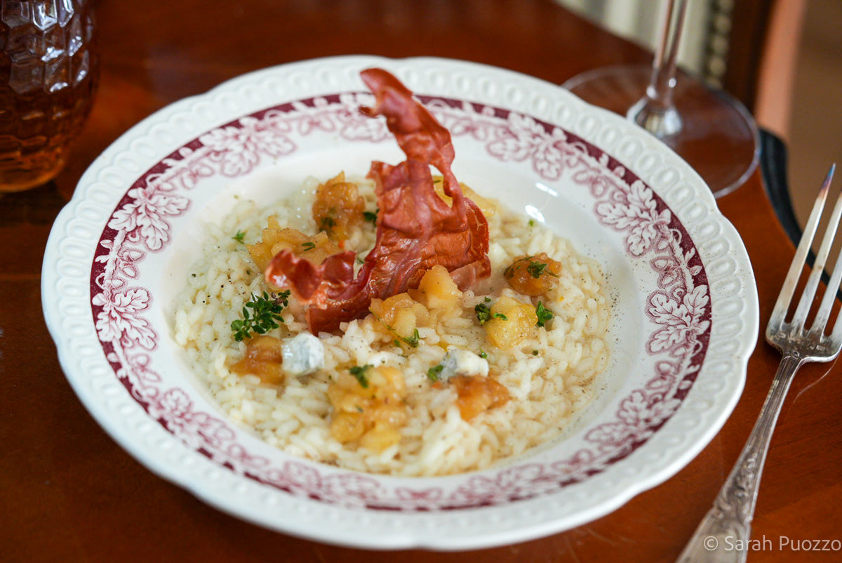 Bord met risotto, peer, gorgonzola en een plakje Parmaham dat recht erin staat