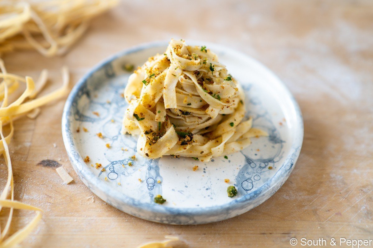 Pastaslierten op een bord met daarbij pangrattato eroverheen. 
